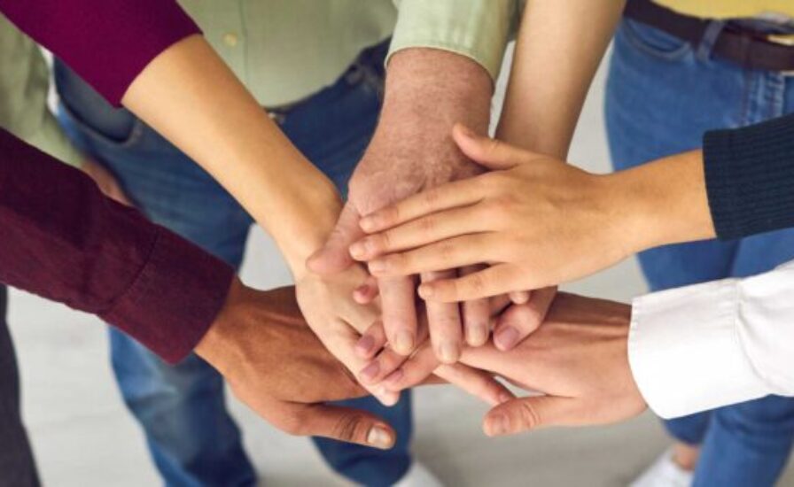 An overhead shot showing a diverse group of people piling their hands one on top of the other, symbolizing teamwork and unity.