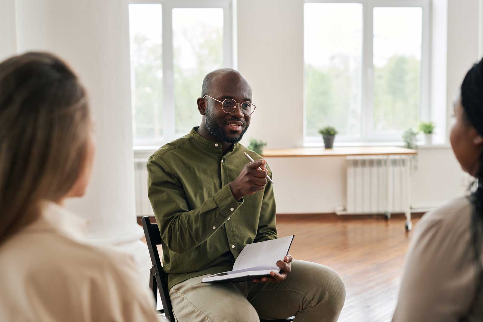 Man with notebook and pen in hand talking to two young women in a light and spacious room
